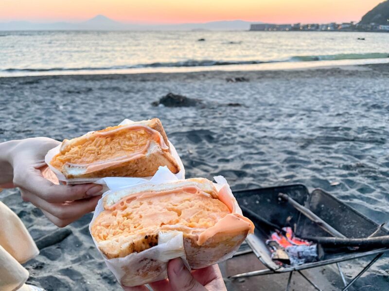 サンダウナートーキョーオムレツのオムレツサンドを海辺で食べている様子